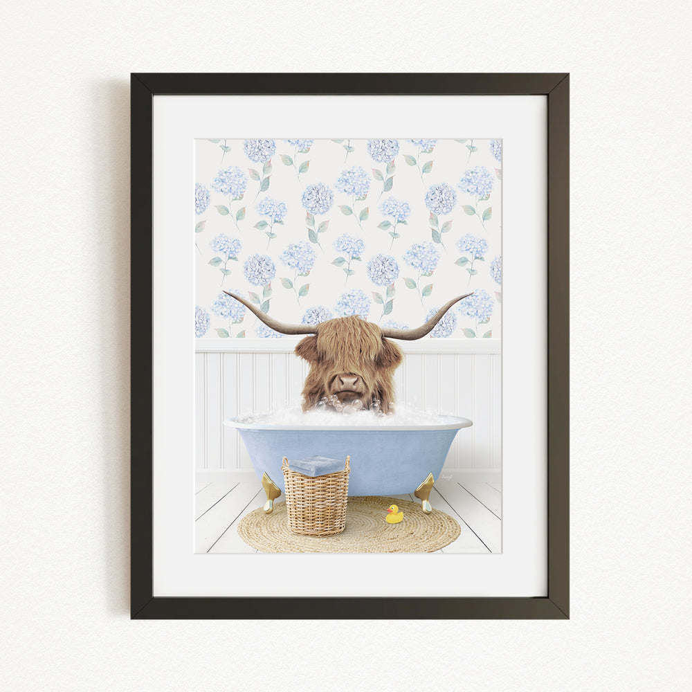 A framed image depicting a Highland cow with long horns sitting in a blue bathtub, surrounded by a floral patterned wall and a basket of rubber ducks.