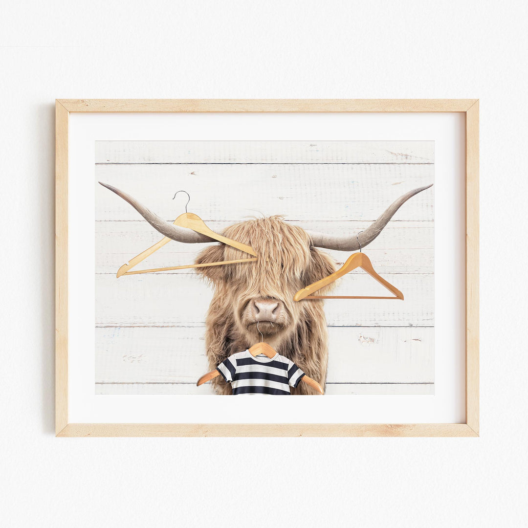 A framed image depicting a large, shaggy-haired animal with a striped shirt, surrounded by hanging clothes hangers.