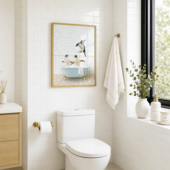 A bathroom with a white toilet, a framed picture of penguins in a bathtub, and a window with greenery on the sill.