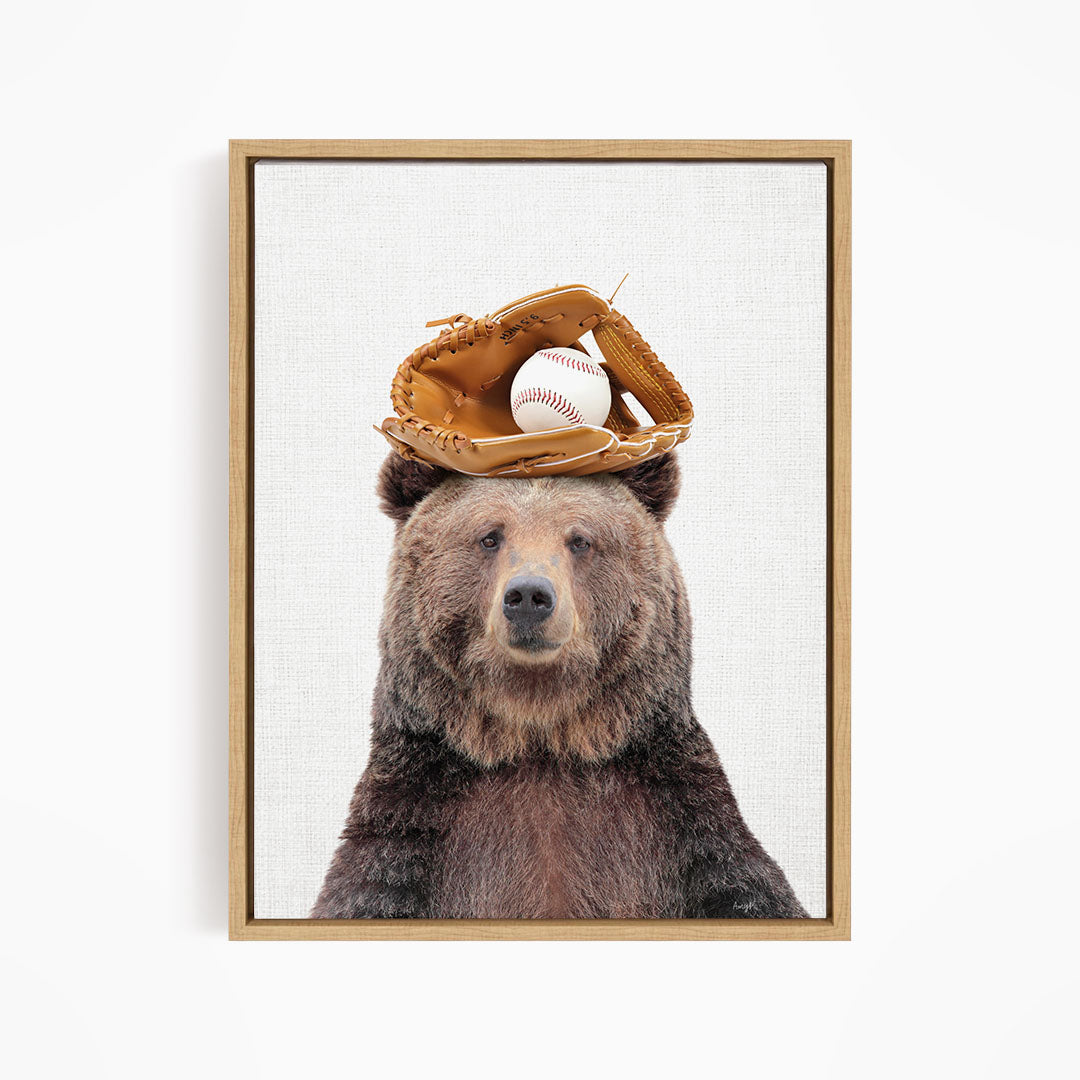 A brown bear wearing a baseball glove on its head, with a baseball resting on top of the glove.