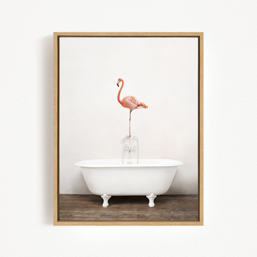 A pink flamingo stands on the edge of a white clawfoot bathtub against a white wall.