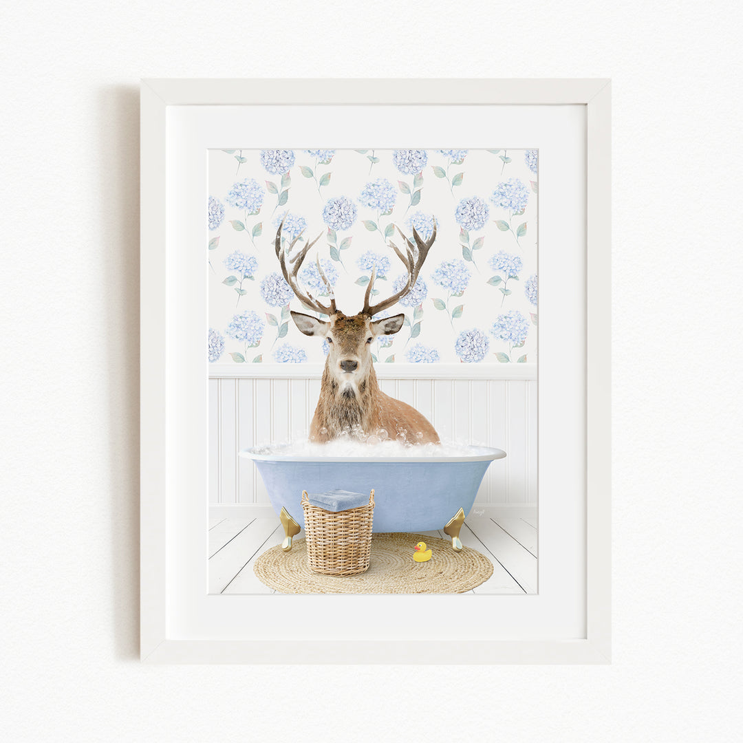 A deer with antlers is sitting in a blue bathtub filled with bubbles, surrounded by a floral patterned wall and a basket of rubber ducks.