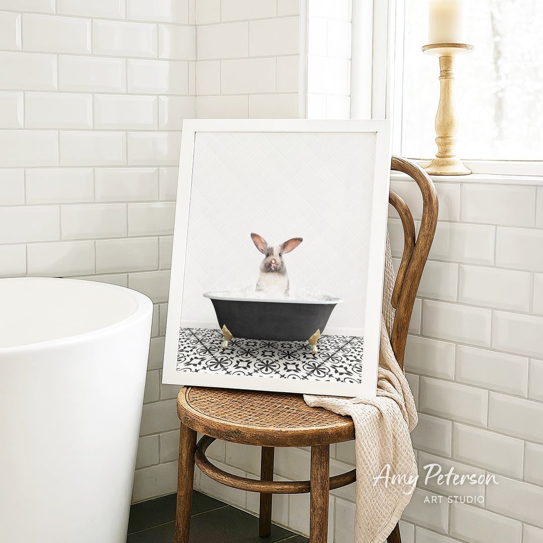 A framed image of a rabbit sitting in a bathtub, surrounded by a patterned tile floor, is displayed on a wooden chair in a bathroom setting.