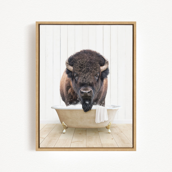 A buffalo with a black mane and horns is sitting in a white bathtub, with its head submerged in the water.