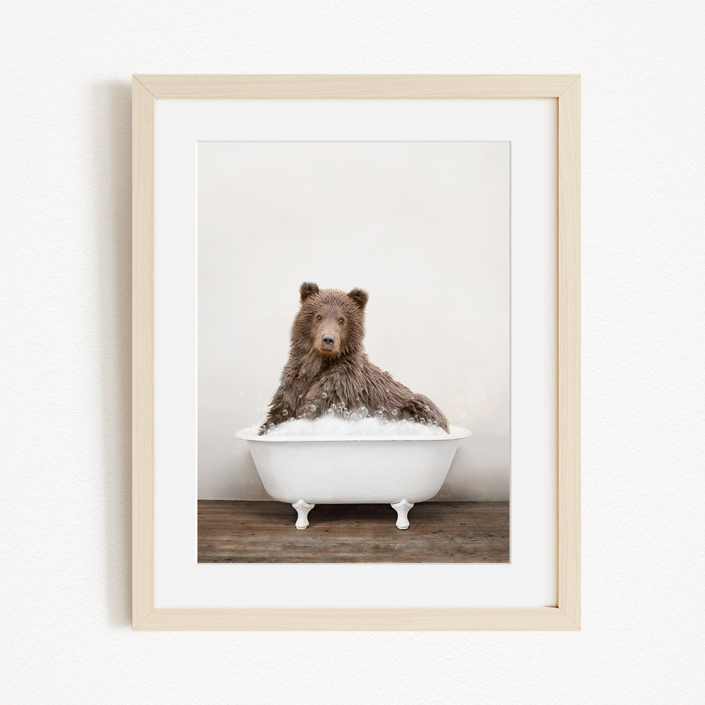 A brown bear sitting in a white bathtub filled with water, looking directly at the camera.