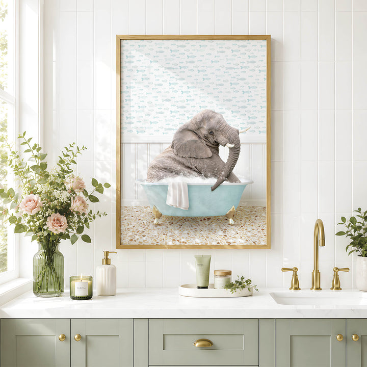A framed image of an elephant sitting in a bathtub, surrounded by flowers and a green vase, is displayed on a white tiled wall above a bathroom sink.