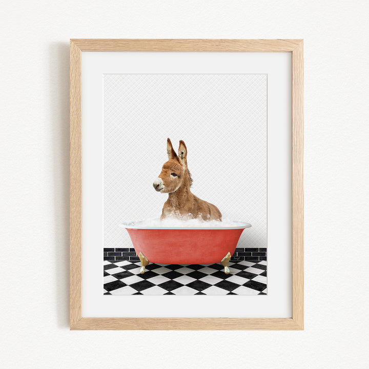A donkey is sitting in a red bathtub filled with water, surrounded by a black and white checkered floor.