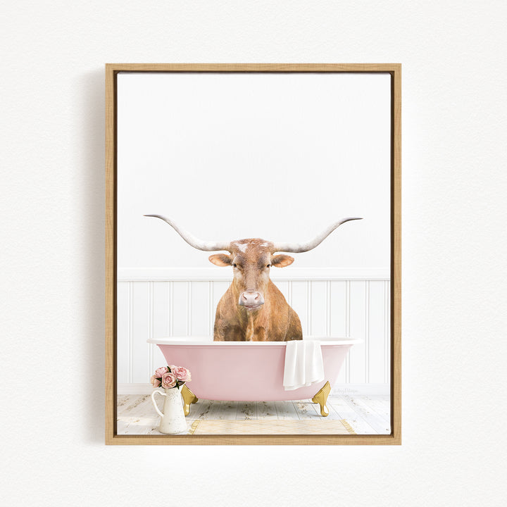 A brown cow with large horns is sitting in a pink bathtub, surrounded by pink flowers and a white vase.