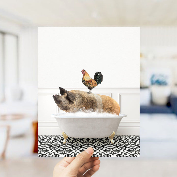 A hand holds up a framed image depicting a pig sitting in a bathtub, with a rooster perched on its back.