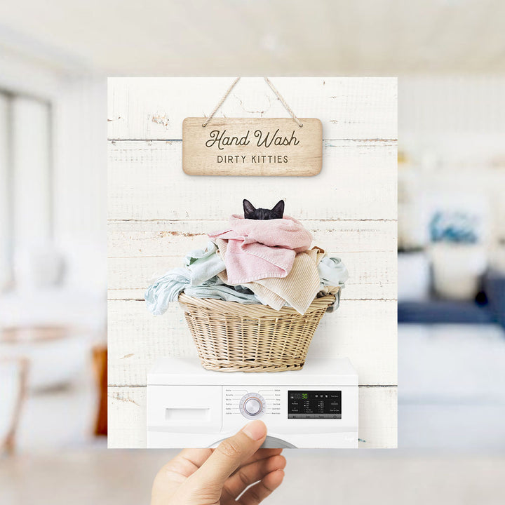 A hand holding a sign that says "Hand Wash Dirty Kitties" above a washer with clothes inside.