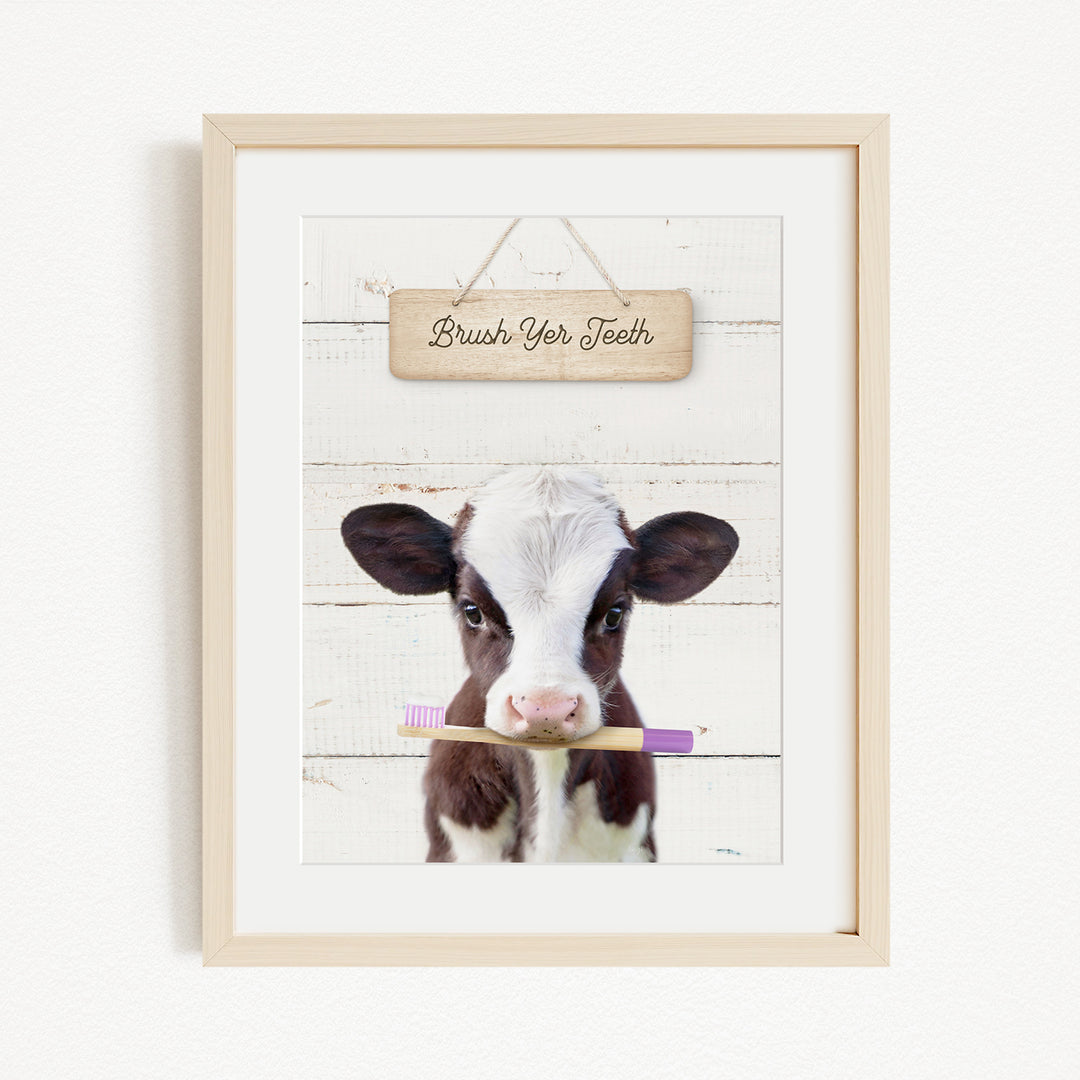 A framed image of a cow holding a toothbrush in its mouth, with a wooden sign above it that says "Brush Your Teeth".