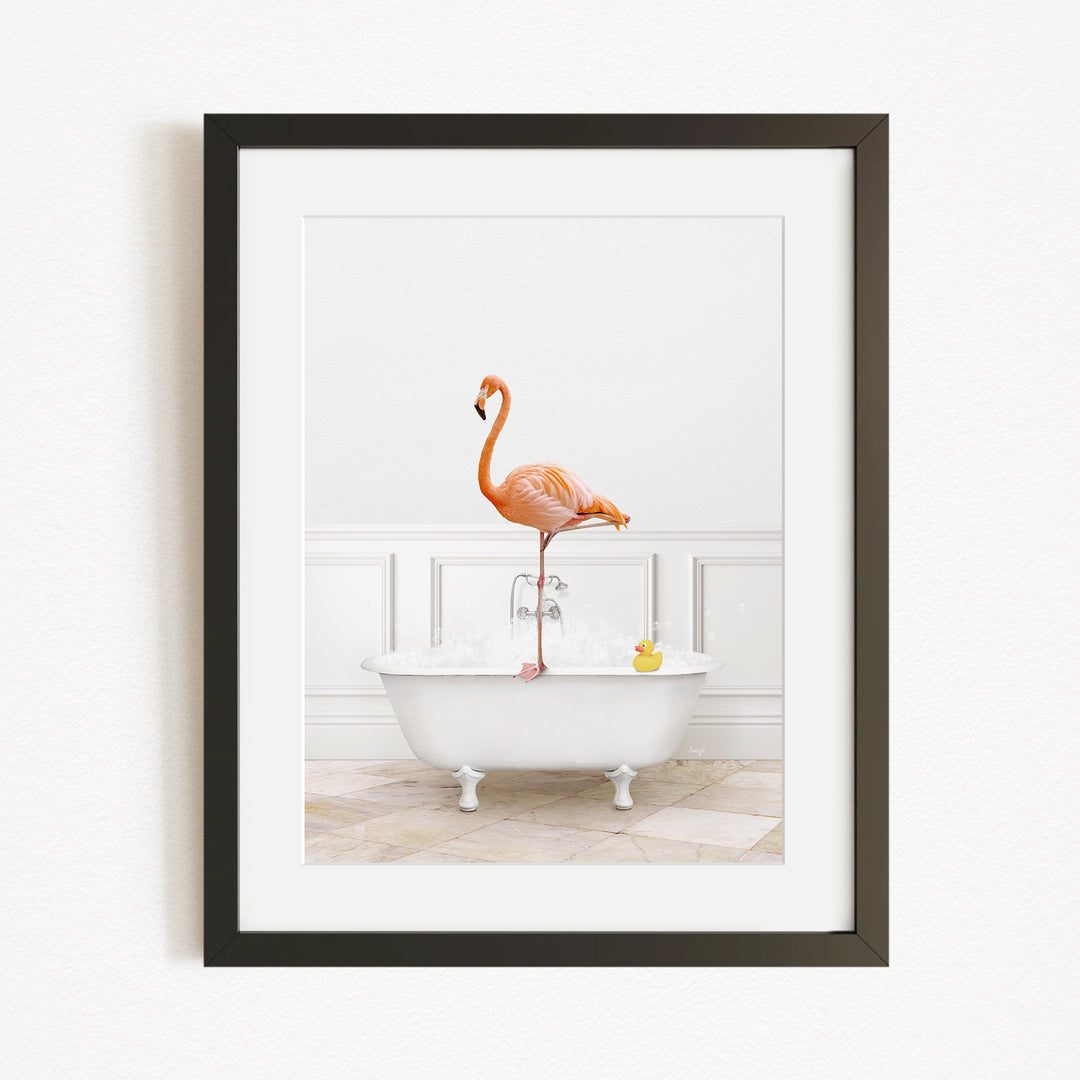 A framed image of a flamingo standing on one leg inside a white bathtub, with a yellow rubber duck floating in the water.