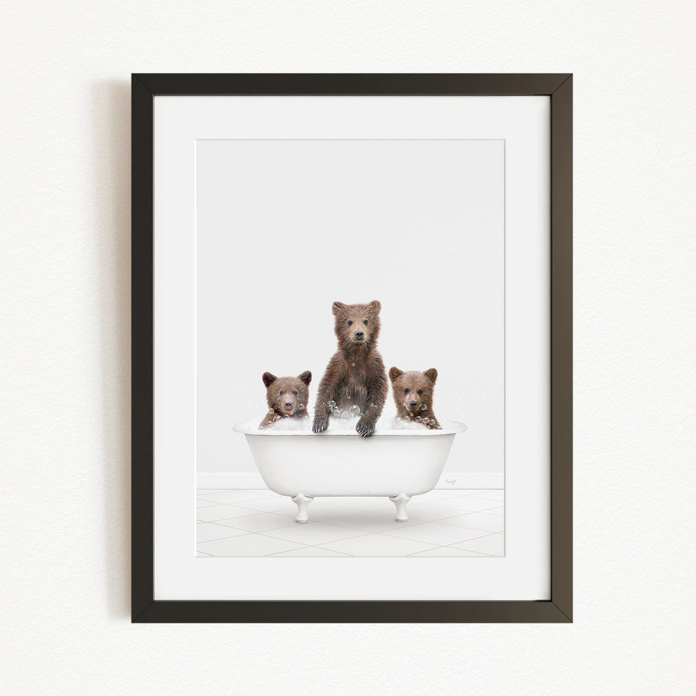 A framed image depicting three brown bears sitting in a white bathtub.