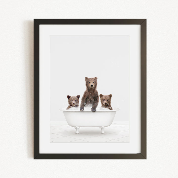 A framed image depicting three brown bears sitting in a white bathtub.