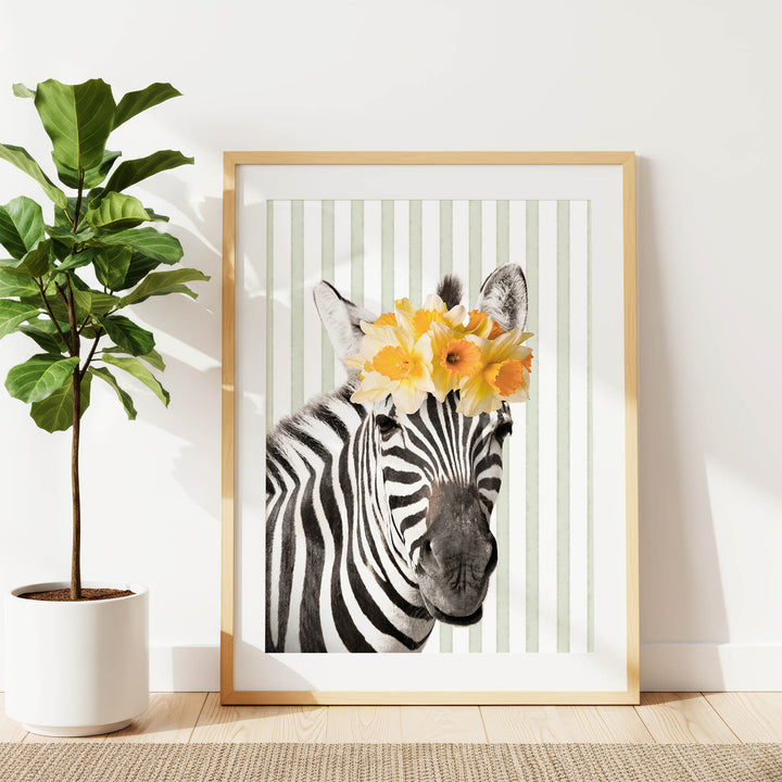 A framed photograph of a zebra wearing a yellow flower crown is displayed on a white wall, with a potted plant to the left.