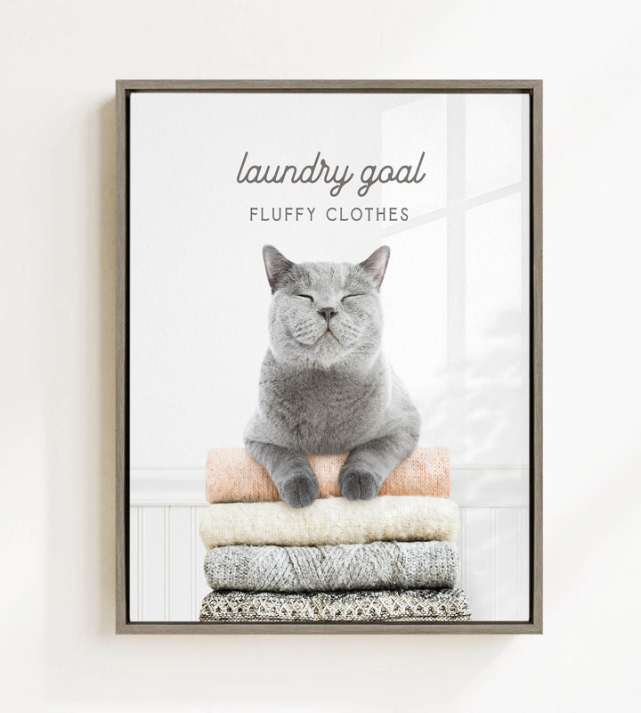A gray cat sitting on a stack of clothes, with the text "laundry goal FLUFFY CLOTHES" above it.