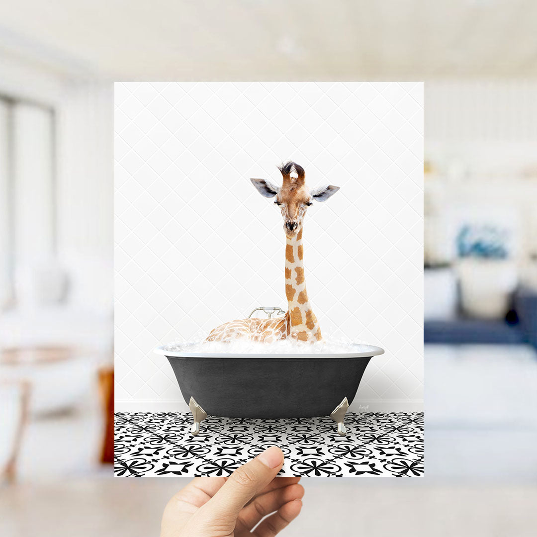 A giraffe sitting in a bathtub filled with bubbles, with a person's hand holding the photo up to the viewer.