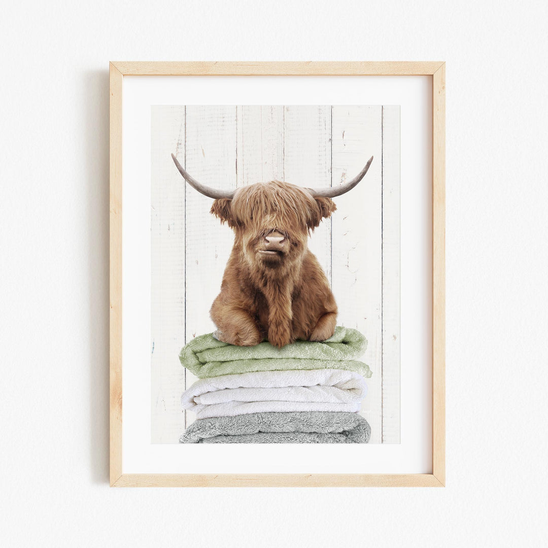 A framed image of a brown, shaggy-haired animal, possibly a yak or a similar creature, sitting atop a stack of towels.