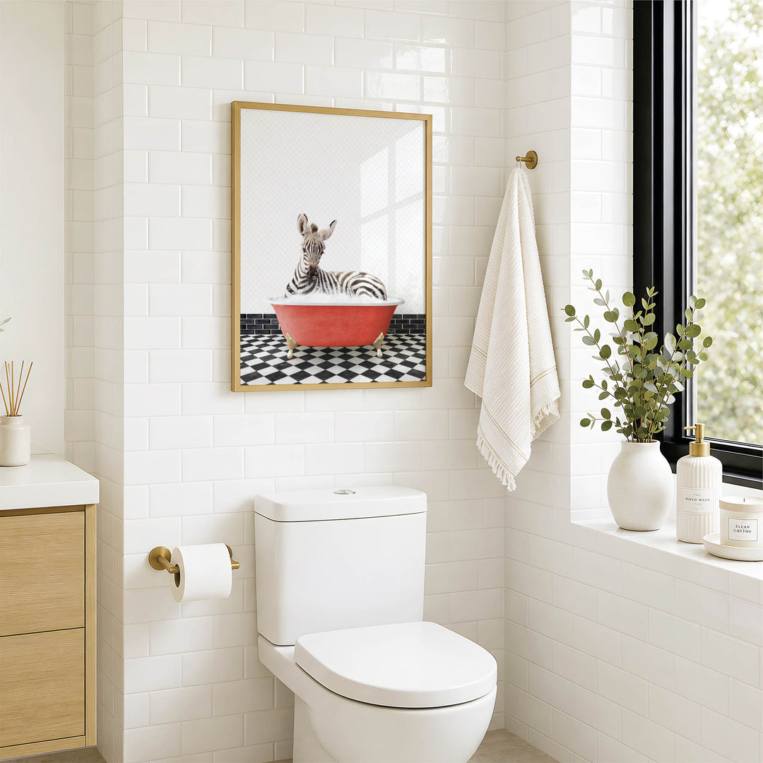 A bathroom with a white toilet, a framed picture of a zebra in a red bathtub, and a window with greenery on the sill.