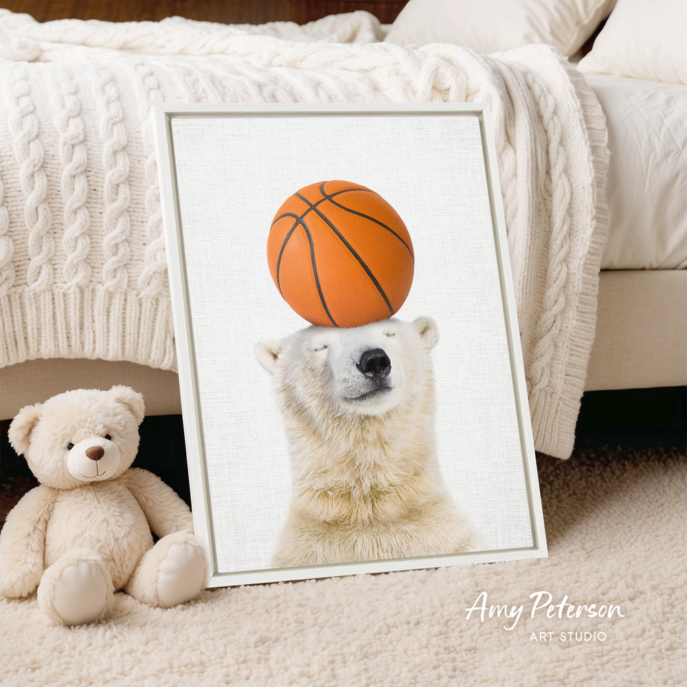 A framed image of a polar bear balancing a basketball on its head, with a teddy bear sitting next to it on a bed.