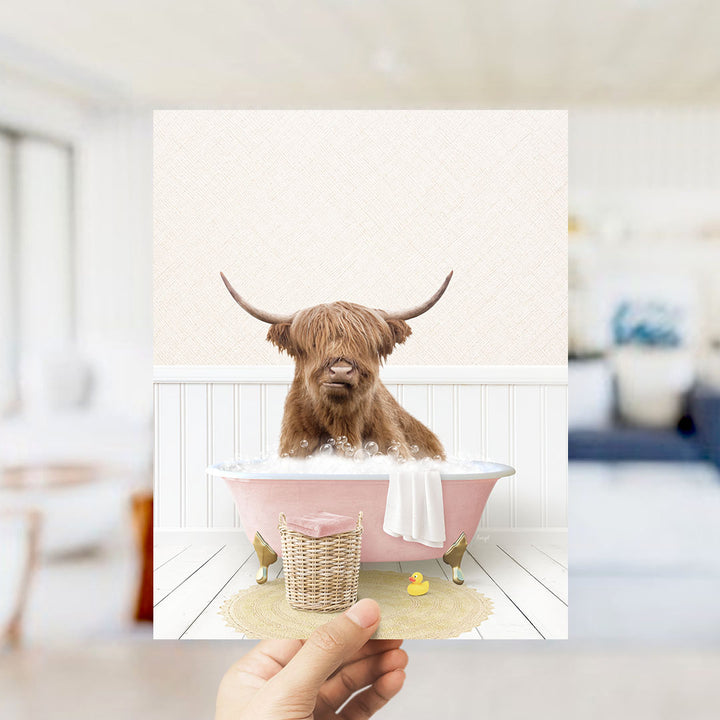 A brown cow with long horns is sitting in a pink bathtub filled with bubbles, surrounded by a yellow rubber duck and a white towel.