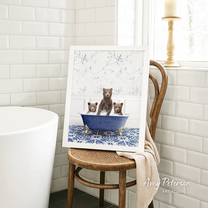 A framed image of three bears sitting in a blue bathtub, with a white tiled wall and a window in the background.