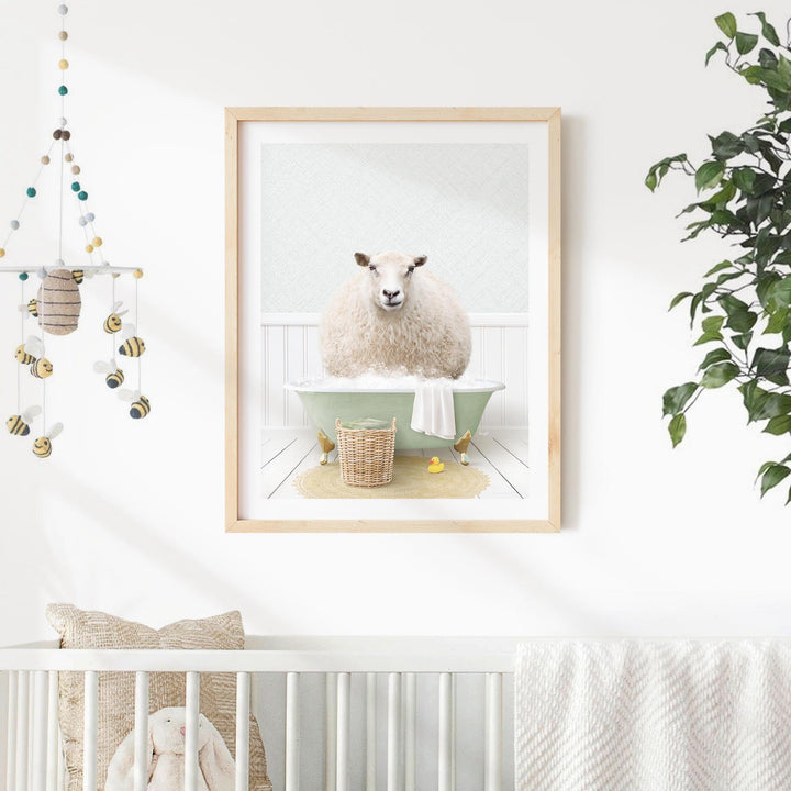 A framed image of a sheep sitting in a bathtub, surrounded by a basket of bath toys, is displayed on a white wall in a nursery setting.