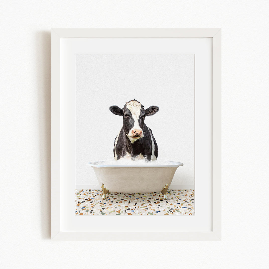 A black and white cow is sitting in a white bathtub filled with water, creating a whimsical and humorous scene.