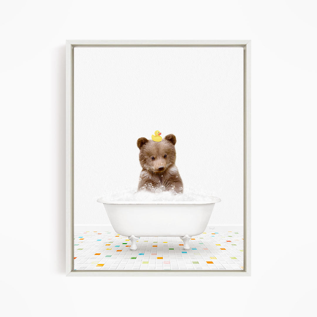 A cute brown bear sitting in a white bathtub filled with bubbles, with a yellow rubber duck perched on its head.