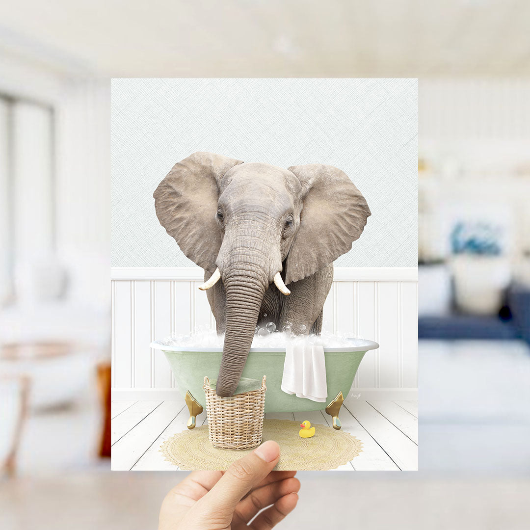 A large gray elephant is sitting in a green bathtub filled with water, surrounded by a yellow rubber duck and a white towel.