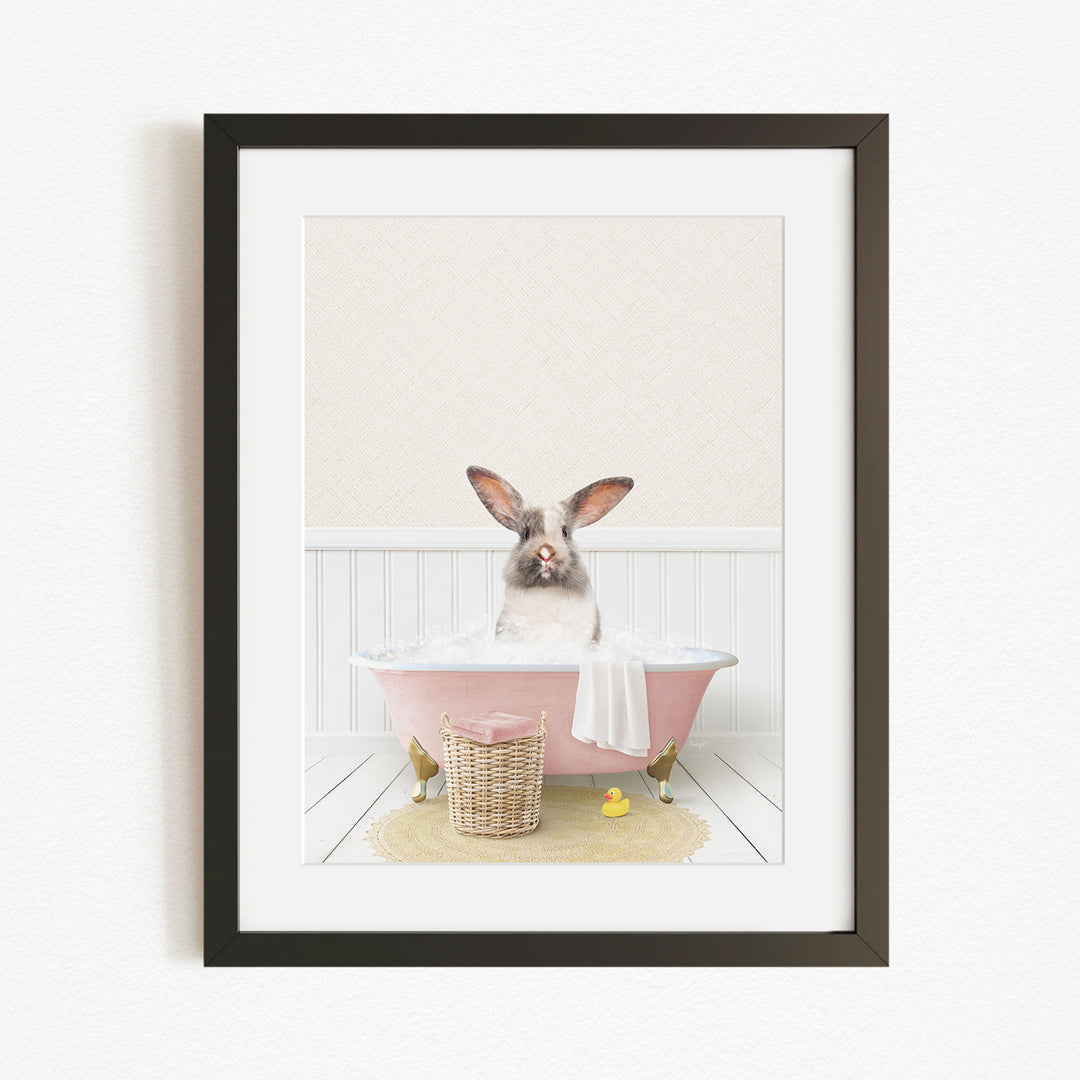 A rabbit sitting in a pink bathtub, surrounded by a yellow rubber duck and a basket of bath toys.