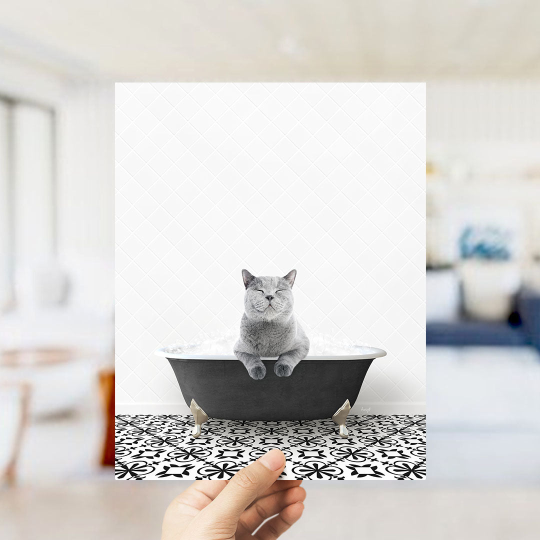 A gray cat sitting in a bathtub filled with bubbles, with a hand holding the image up to the camera.