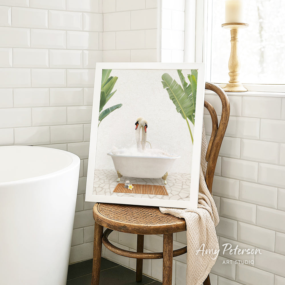 A framed image of a dog sitting in a bathtub, surrounded by tropical plants, is displayed on a wooden chair in a bathroom setting.