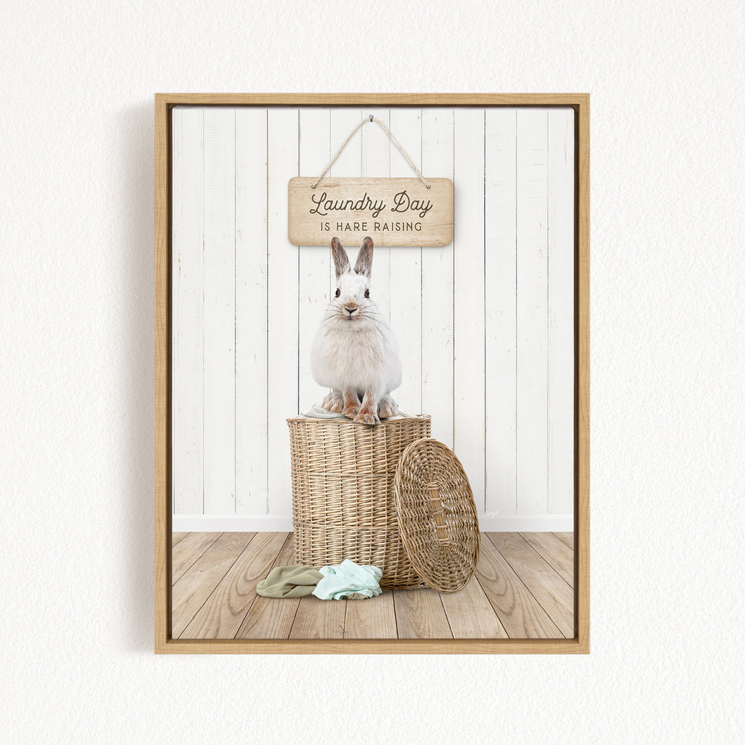 A white rabbit sits atop a wicker basket, with a wooden sign above that reads "Laundry Day is hard raising".