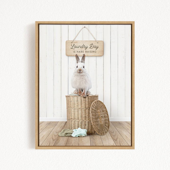 A white rabbit sits atop a wicker basket, with a wooden sign above that reads "Laundry Day is hard raising".