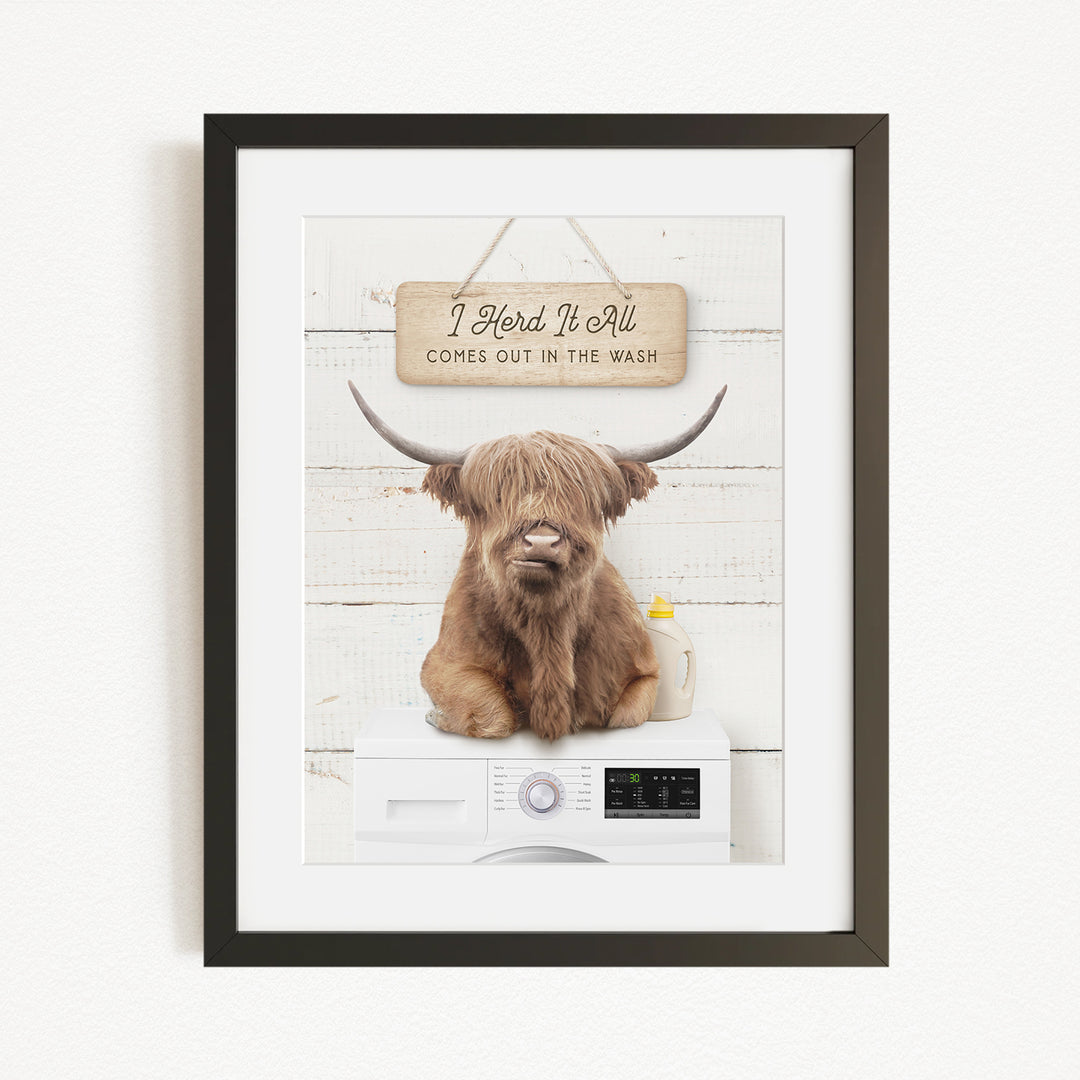 A framed image of a Highland cow with large horns sitting on a washing machine, with a sign above that says "I herd it all comes out in the wash".