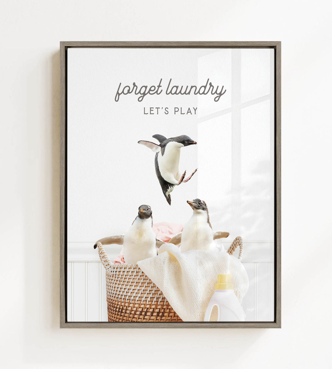 A framed image depicting three penguins in a basket, with the text "forget laundry, let's play" written above them.