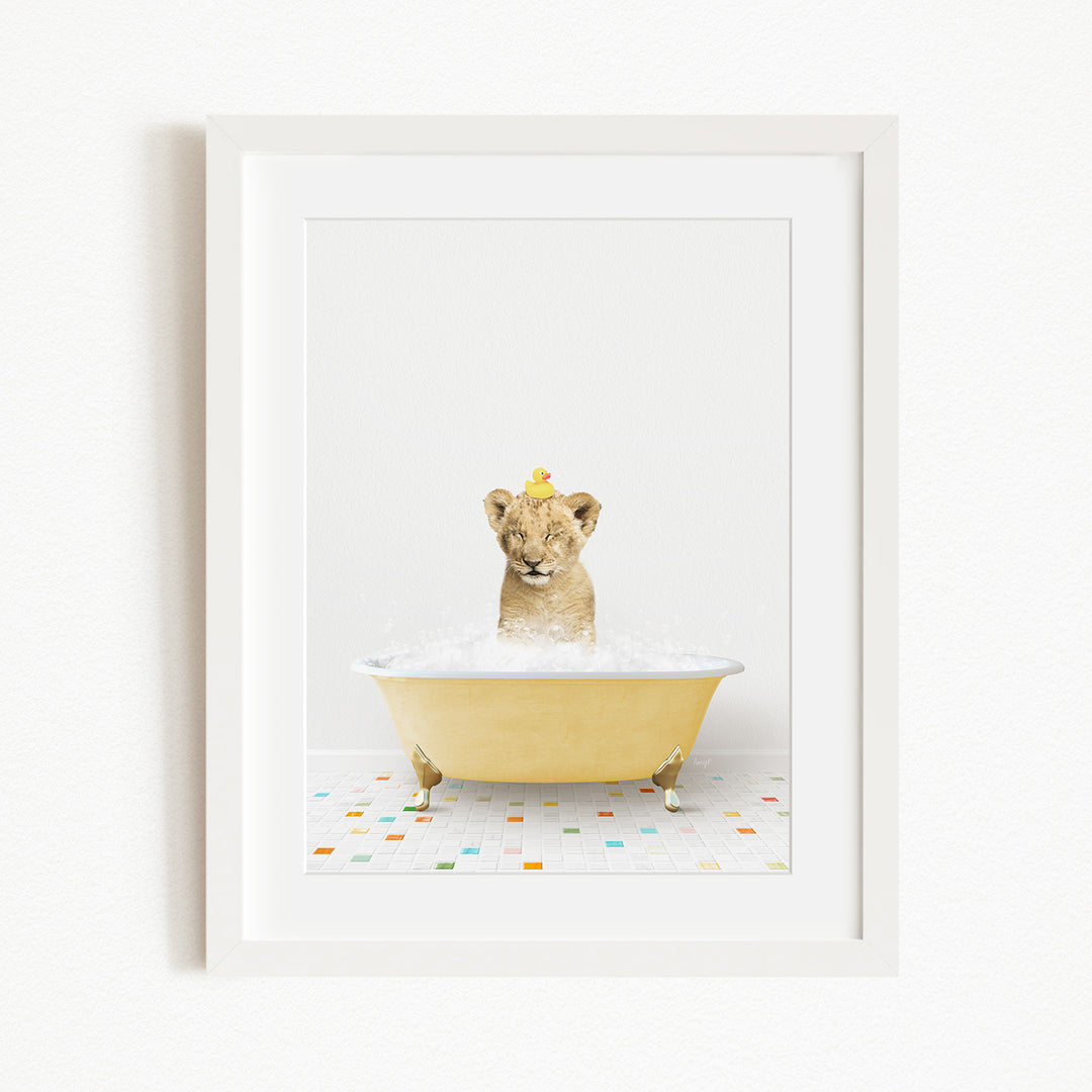 A young lion cub sitting in a yellow bathtub filled with bubbles, with a yellow rubber duck floating on the water.