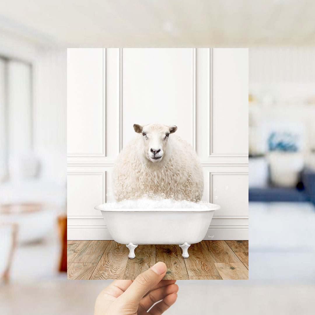A fluffy white sheep sits in a white bathtub filled with bubbles, with a blurred background suggesting a bathroom setting.
