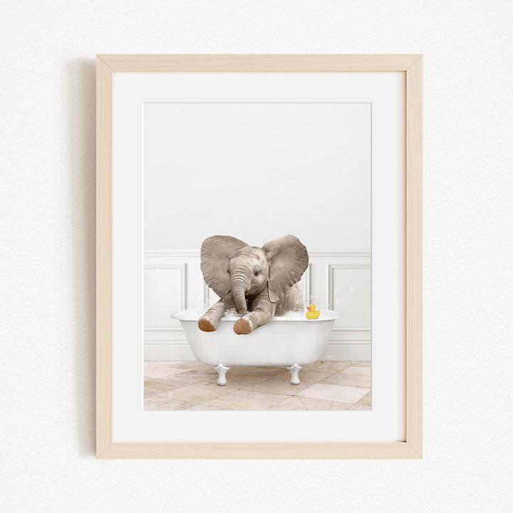 A baby elephant sitting in a white bathtub, with a yellow rubber duck floating nearby.