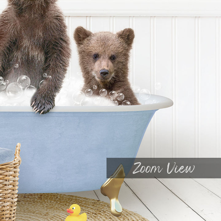 A baby bear sitting in a bathtub filled with bubbles, with a yellow rubber duck nearby.