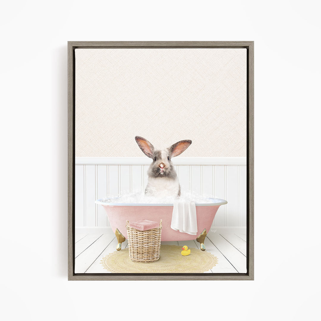 A fluffy white rabbit sits in a pink bathtub filled with bubbles, surrounded by a yellow rubber duck and a wicker basket.