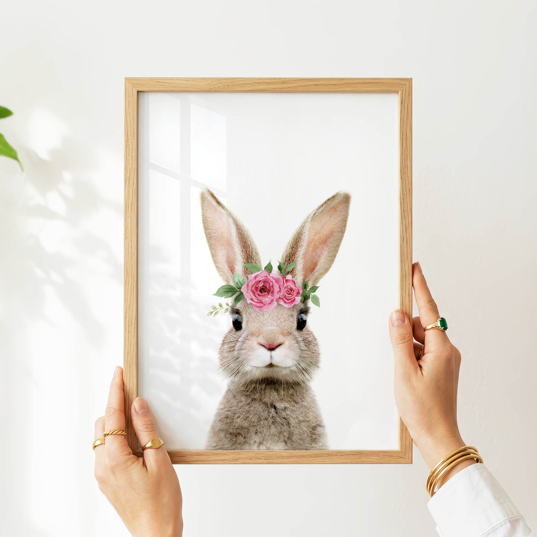 A person's hands are holding a wooden frame with a picture of a rabbit wearing a pink flower crown.