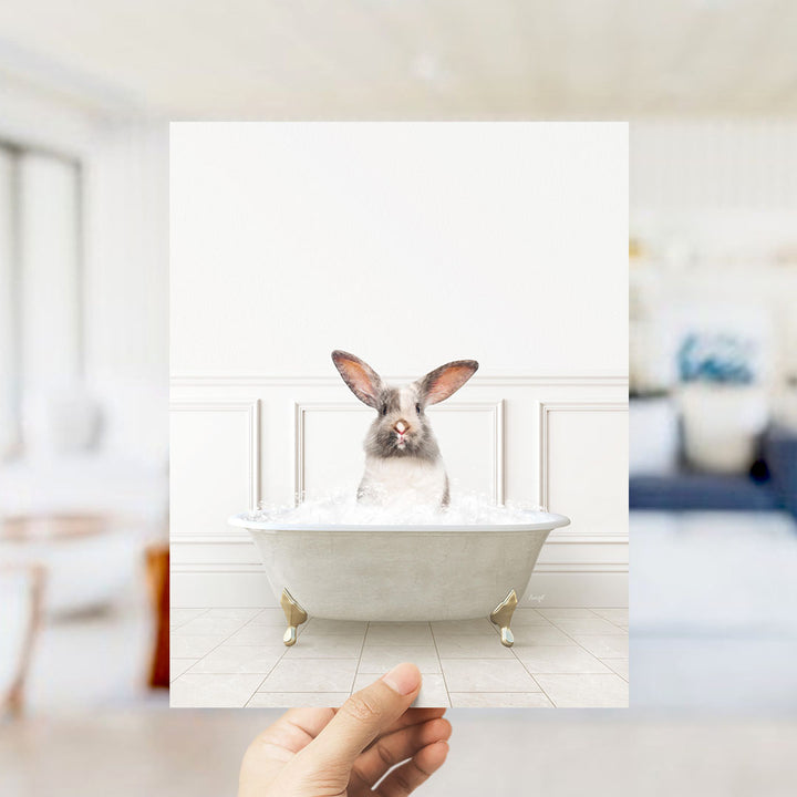 A hand holds up a framed image of a rabbit sitting in a bathtub filled with water, with a blurred background suggesting a bathroom setting.