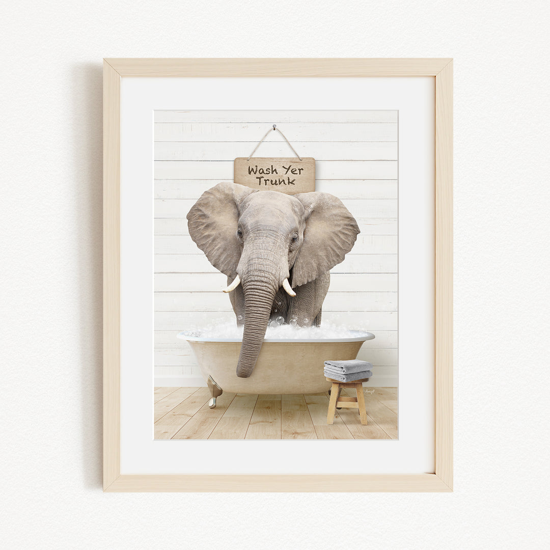 A framed image of an elephant standing in a bathtub, with a sign above it that says "Wash Yer Trunk".
