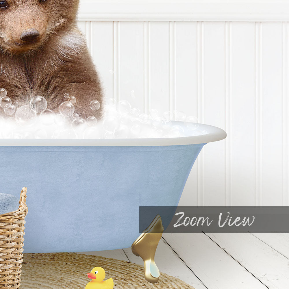 A small brown bear is sitting in a blue bathtub filled with bubbles, surrounded by a yellow rubber duck and a basket.