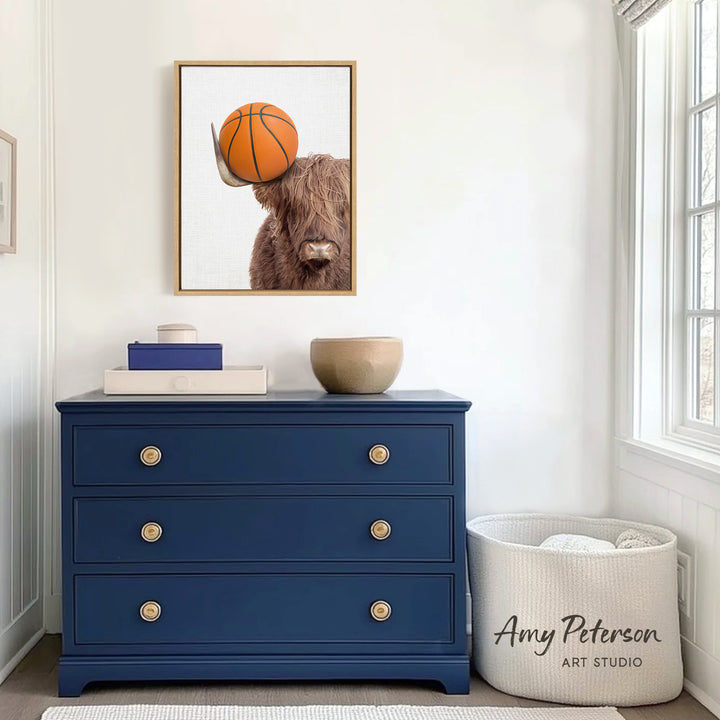 a blue dresser with a framed picture of a cow holding a basketball on top of it. The dresser is situated in a room with a window and a white basket.
