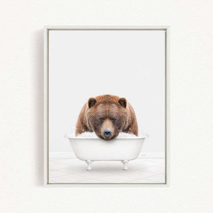 A brown bear sitting in a white bathtub filled with bubbles, looking directly at the camera.