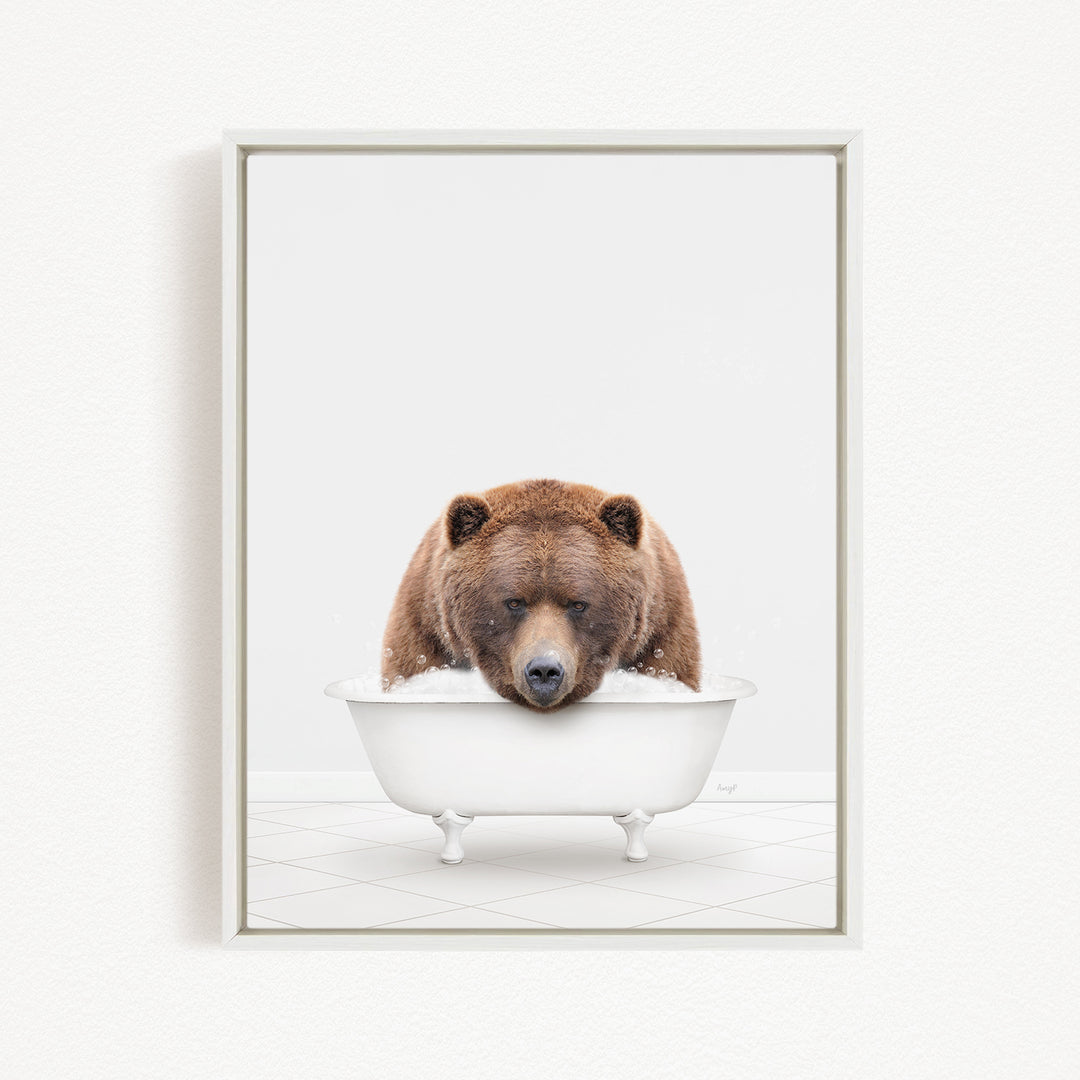 A brown bear sitting in a white bathtub filled with bubbles, looking directly at the camera.