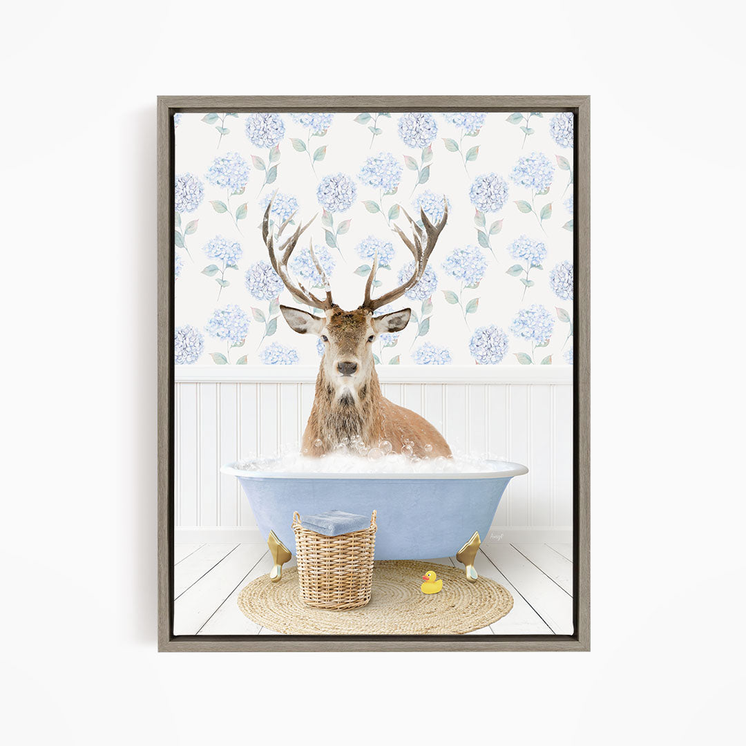 A deer with antlers is sitting in a blue bathtub filled with water, surrounded by a wicker basket and yellow rubber ducks.